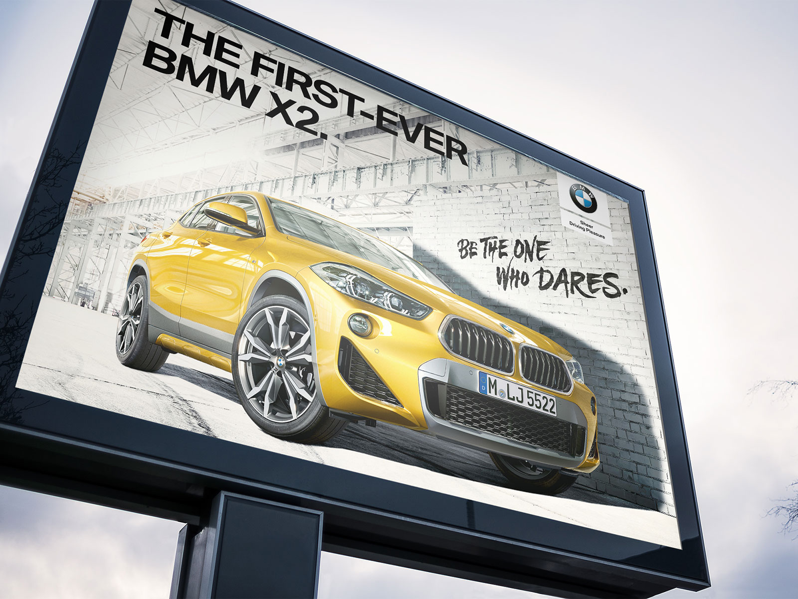 BMW Megalight-Plakat im Hochformat: Gelber X2 vor Backsteinwand, Headline „The First-Ever BMW X2. Be The One Who Dares."