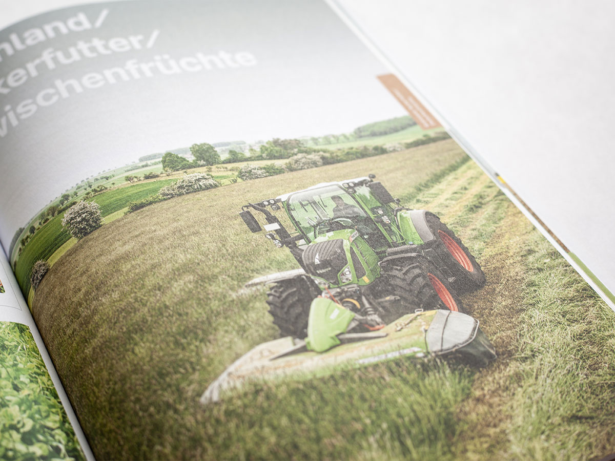 Aufgeschlagene Broschürenseite mit Kapitel Grünland/Ackerfutter/Zwischenfrüchte: Fendt-Traktor bei der Mahd auf einer Wiese.