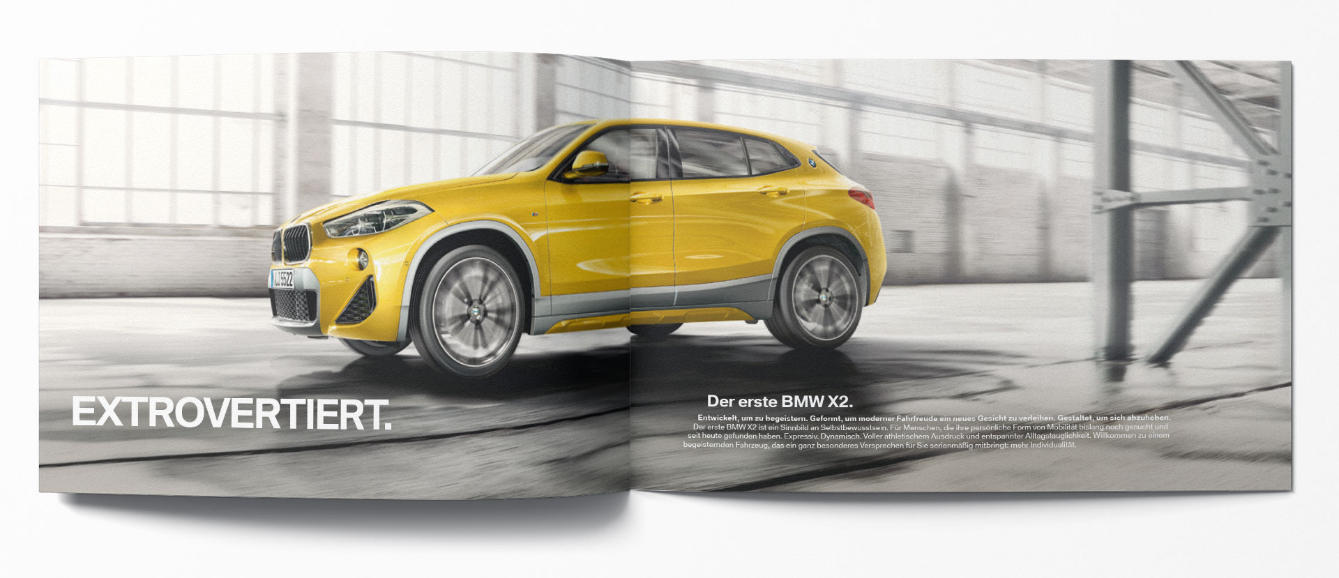 Aufgeschlagene BMW X2 Broschüren-Doppelseite: Gelber X2 in Industriehalle, Headline „Extrovertiert." links, Einführungstext rechts.